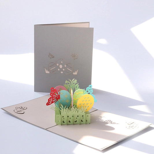 Closed beige Easter card cover with an elegant laser-cut design of an egg and butterflies, resting on a white knitted surface with flowers.