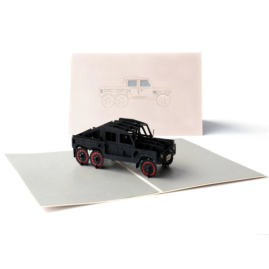 Front view of a 3D pop-up greeting card featuring a black 6x6 off-road truck model standing on a grey base, with a line drawing of the truck on the pink cover behind it.