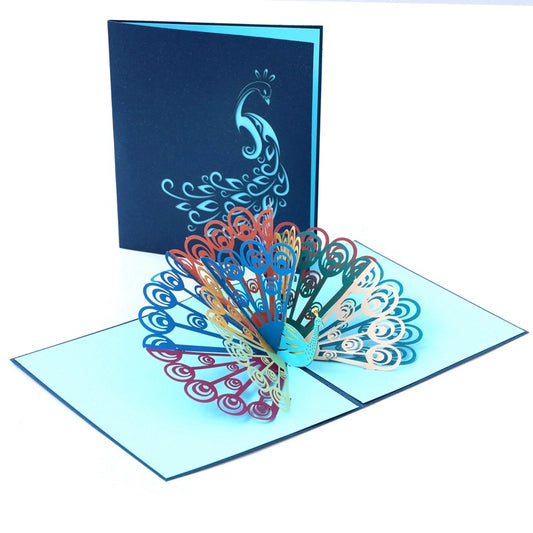 Open peacock pop-up greeting card next to dark blue cover with silver peacock silhouette design
