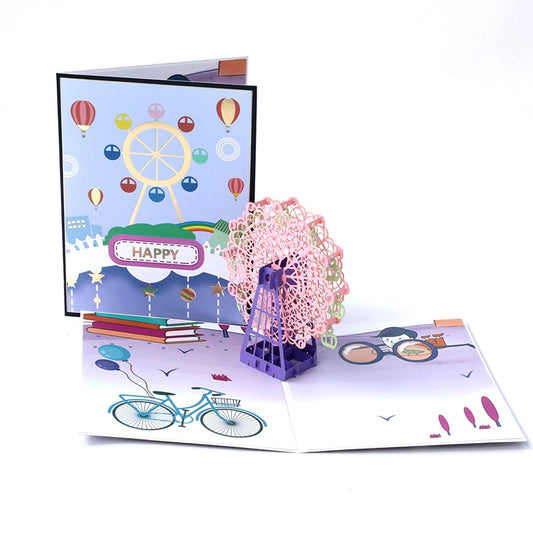 Front cover of the 3D card featuring a cartoon Ferris wheel, rainbow, and hot air balloons on light blue background.