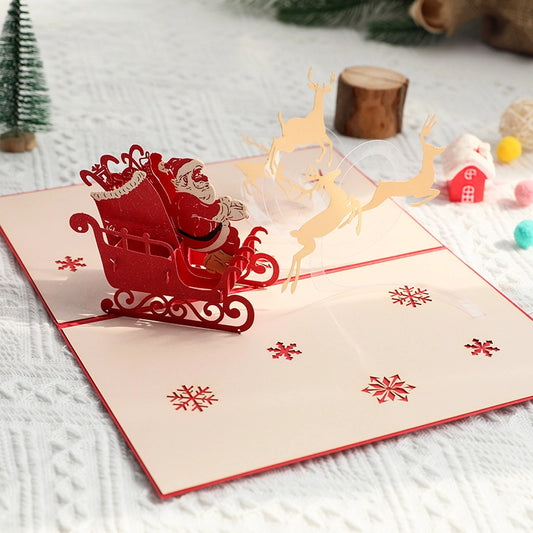 3D pop-up Christmas card featuring Santa Claus in a red sleigh pulled by golden reindeer, opened against a red background with a moon silhouette.