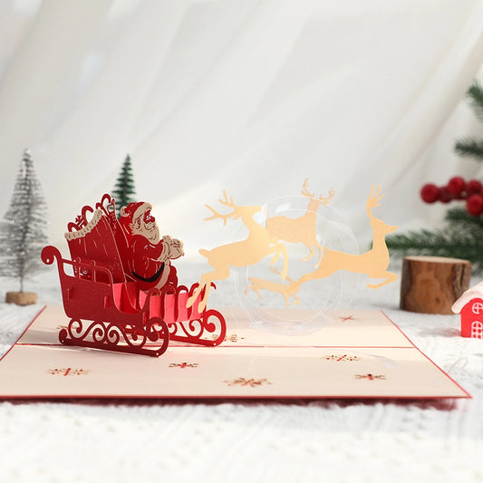 Festive holiday scene with a 3D Santa pop-up card on a white table, surrounded by mini Christmas trees and red berries.