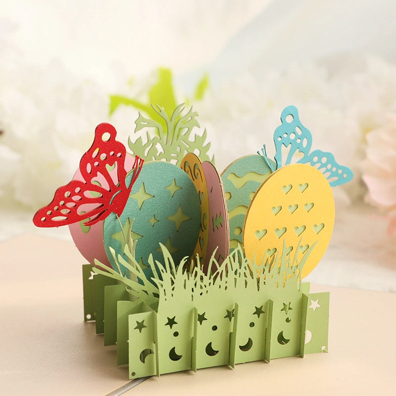 Close-up detail of the 3D Easter card showing intricate laser-cut patterns on the yellow and blue eggs, green grass blades, and red butterfly wings.