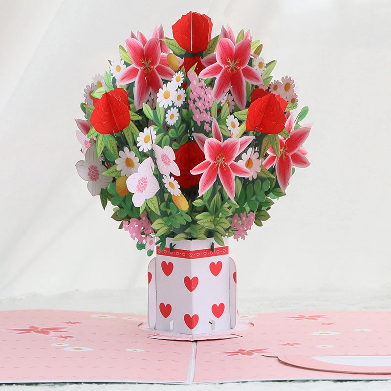Close-up detail of paper art red roses, pink lilies, and daisies standing upright in a heart-patterned vase