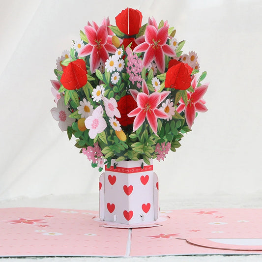 Close-up detail of paper art red roses, pink lilies, and daisies standing upright in a heart-patterned vase