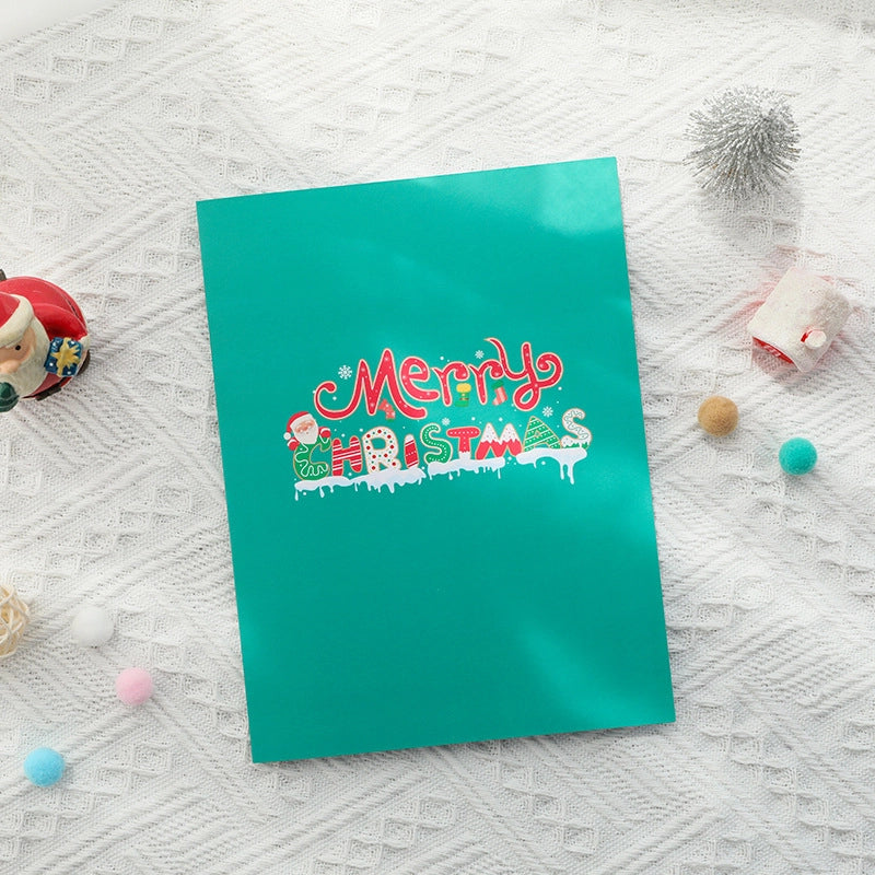 Closed teal Christmas card cover featuring colorful "Merry Christmas" lettering with snow and Santa details.