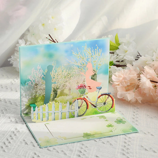 Side view of a 3D pop-up wedding card featuring a vintage bicycle with flowers and a couple silhouette under spring trees.