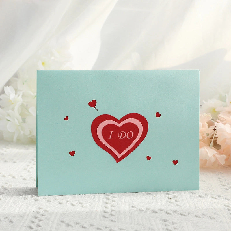 Light blue greeting card cover with a red heart cutout saying "I DO" surrounded by small hearts.