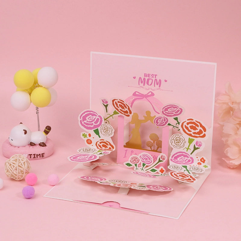 Close up of Best Mom pop-up card featuring intricate paper cut carnations in pink and orange with a central gold mother and child silhouette
