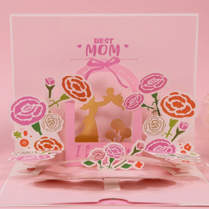 Close up of Best Mom pop-up card featuring intricate paper cut carnations in pink and orange with a central gold mother and child silhouette
