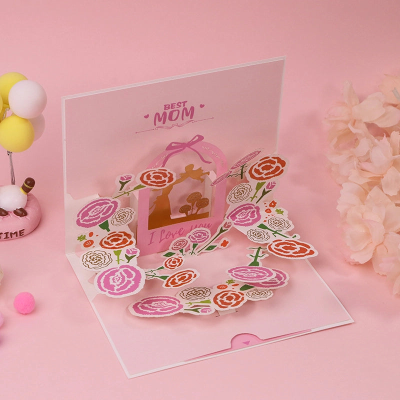 Close up of Best Mom pop-up card featuring intricate paper cut carnations in pink and orange with a central gold mother and child silhouette

