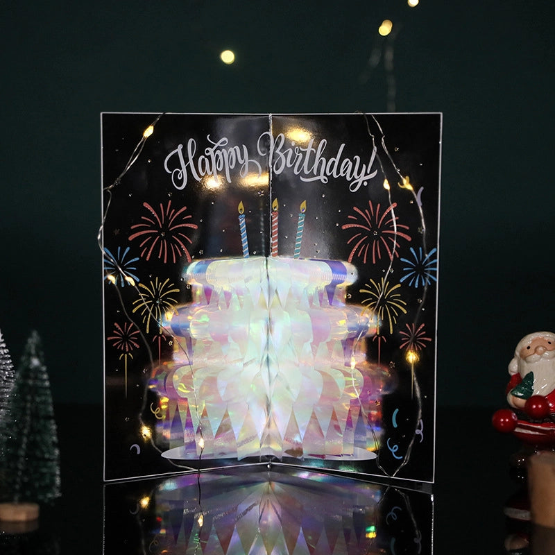 Holographic birthday cake pop-up card displayed with festive lights