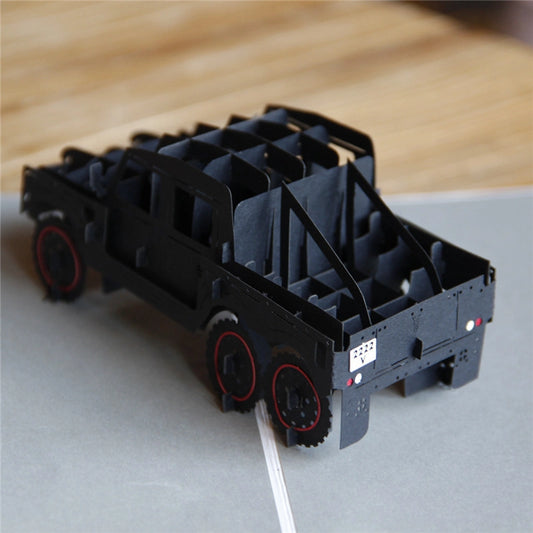 Side angle close-up of the black paper craft truck card, highlighting the red wheel details, license plate, and intricate layered construction on a wooden table.