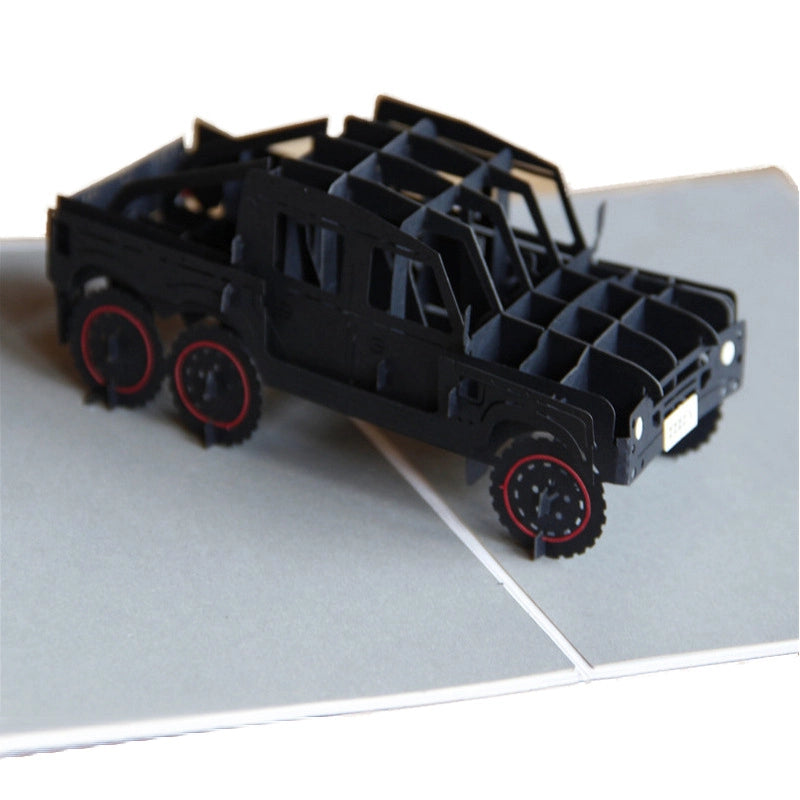 Close-up side profile of the 3D paper truck model, emphasizing the suspension details, window cutouts, and the six-wheel drive design.