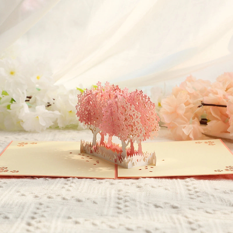 Detailed shot of the laser-cut cherry blossom trees in the 3D card, highlighting the layered pink petals and white trunk design, with soft natural lighting enhancing the card's elegant craftsmanship.