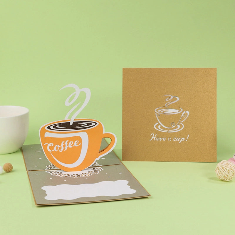 3D pop-up greeting card featuring an orange coffee cup with steam rising from it on a lace doily background.
