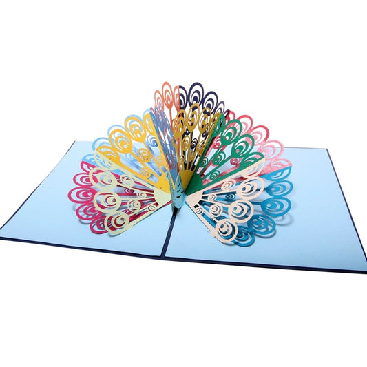 Front view of colorful peacock 3D pop-up card with rainbow feathers fully fanned out on light blue background
