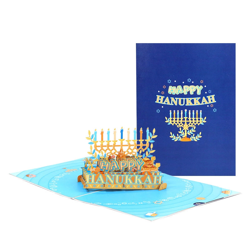 Dark blue Happy Hanukkah card cover with gold foil menorah design and matching yellow envelope on green background