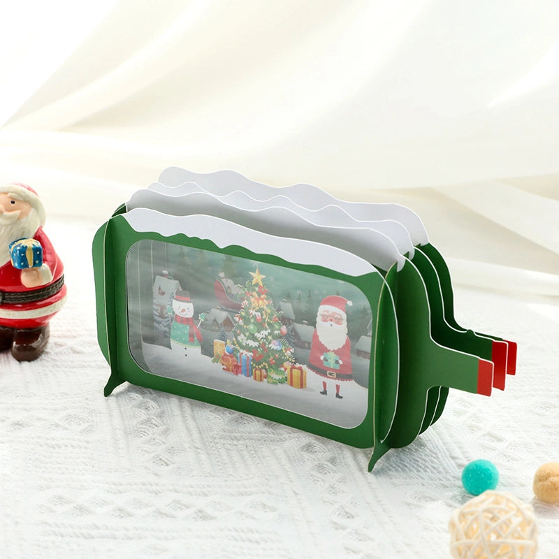 Side angle of the 3D Christmas TV card on a white table, highlighting the red pull-tab lever used to animate the scene inside.