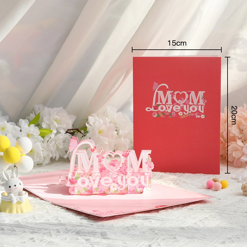 Mom Love You 3D pop-up card open showing pink floral lettering and butterfly, size 15x20cm, red cover in background
