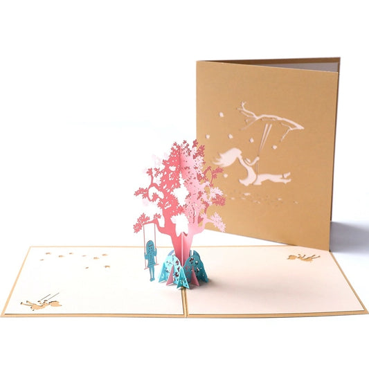 Front view of intricate pink paper tree pop-up card with detailed branch cutouts and blue base
