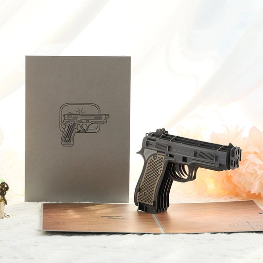 Grey greeting card cover with minimalist pistol line art design resting on a yellow envelope, creative gift stationery
