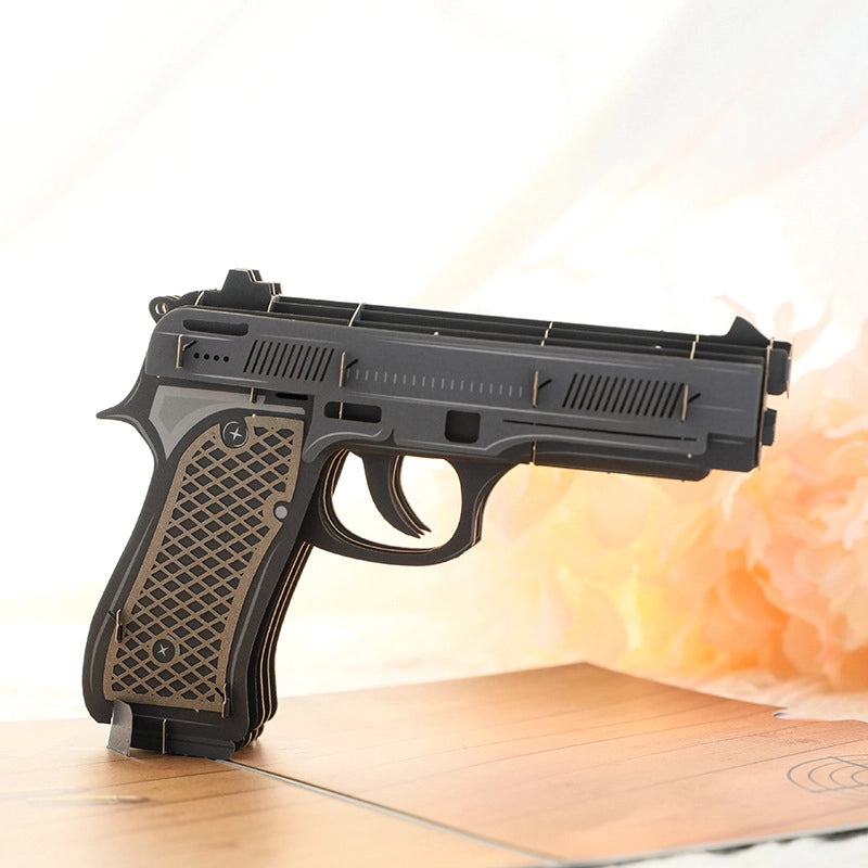 Close up side view of black and brown layered paper cut gun model, showing intricate 3D construction and grip texture details
