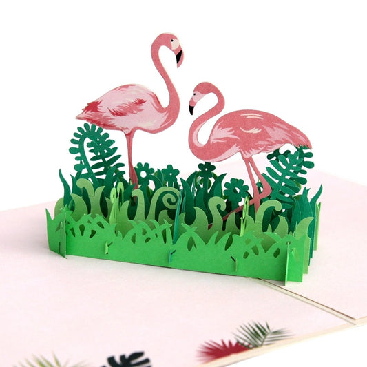 Close-up view of the 3D paper cut flamingos with detailed pink feathers and black beaks, surrounded by intricate green fern and grass layers.