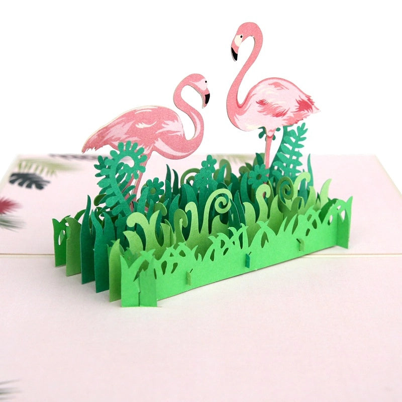 Side angle of the open flamingo card highlighting the layered paper construction of the green vegetation and the standing posture of the pink birds.