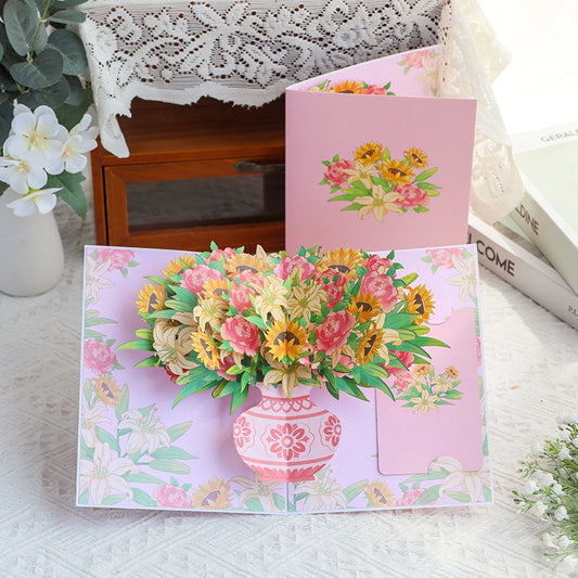 Open 3D flower vase pop-up card displayed next to closed pink cover on white table
